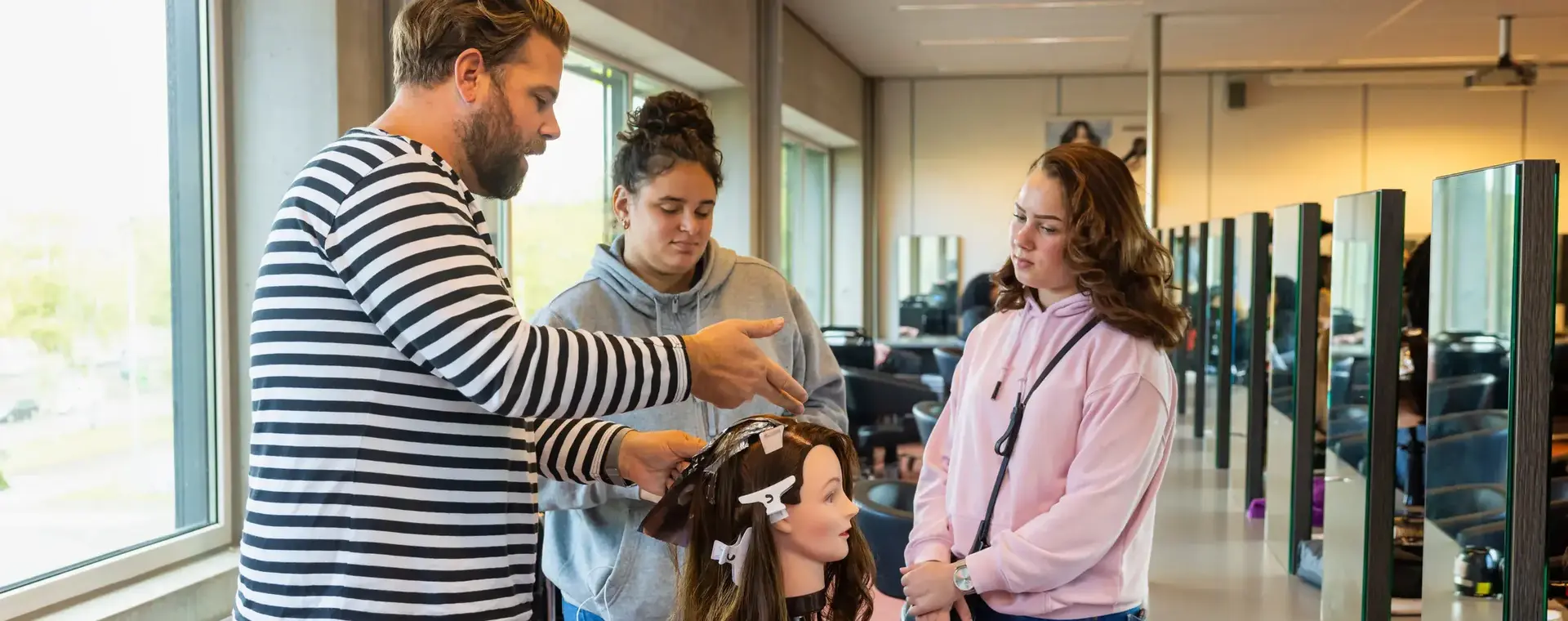 Studenten oefenen haarverzorging onder begeleiding in de salonschool.