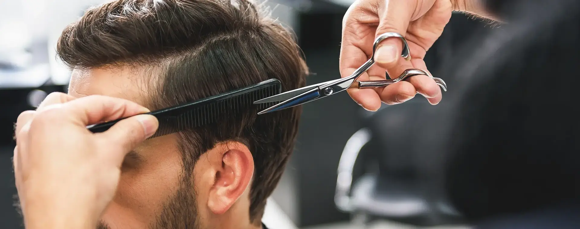 Kapster knipt het haar van een man met een tondeuse en kam in een moderne kapsalon. De klant zit stil terwijl het haar nauwkeurig in model wordt gebracht.