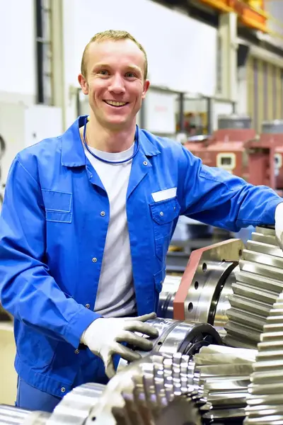 Man in blauwe overall bij tandwielvormige objecten