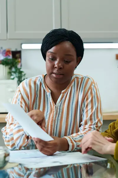 Twee vrouwen zitten aan een keukentafel en bespreken samen documenten. De jongere vrouw legt iets uit aan de oudere vrouw.