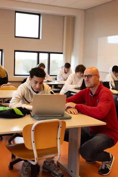 Docent helpt leerling met laptop in klaslokaal
