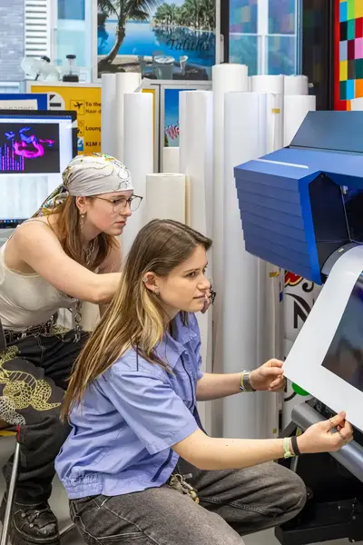 Twee studentes halen een glossy kleurenafdruk uit een professionele printer.