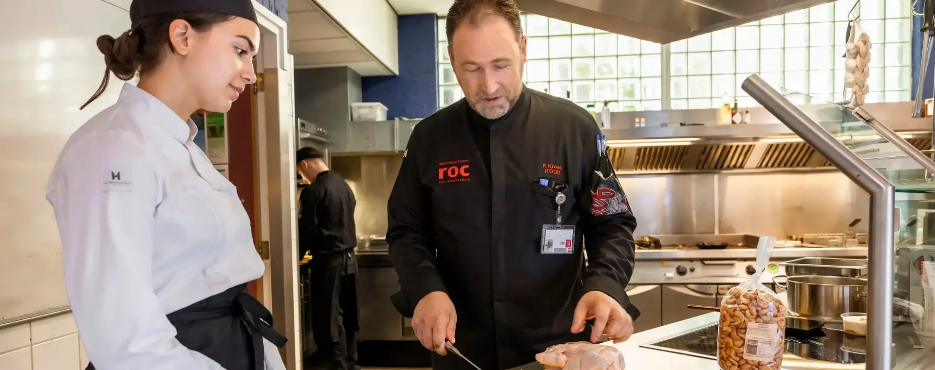 Docent legt student uit hoe vlees gesneden wordt in professionele keuken.