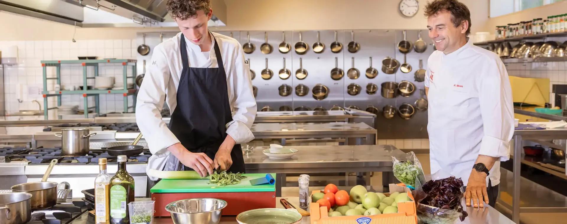 Student en docent bereiden samen een maaltijd in professionele keuken.