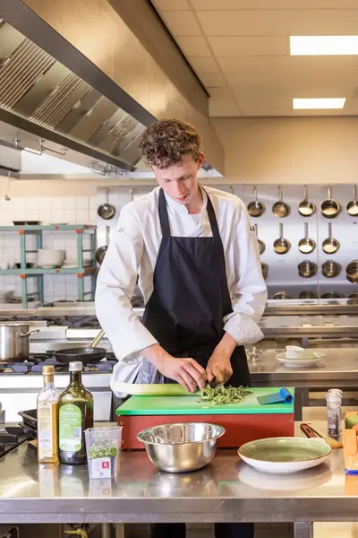 Student en docent bereiden samen een maaltijd in professionele keuken.