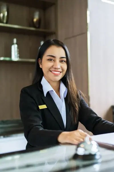 Een receptioniste in een zwart pak met wit overhemd zit achter de balie.