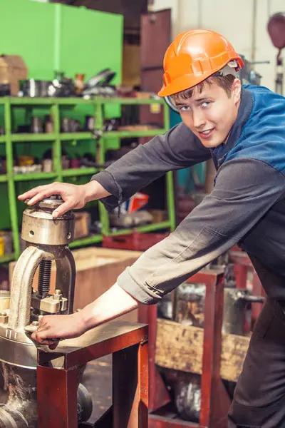Monteur met oranje veiligheidshelm werkt met een industriële machine in een werkplaats.