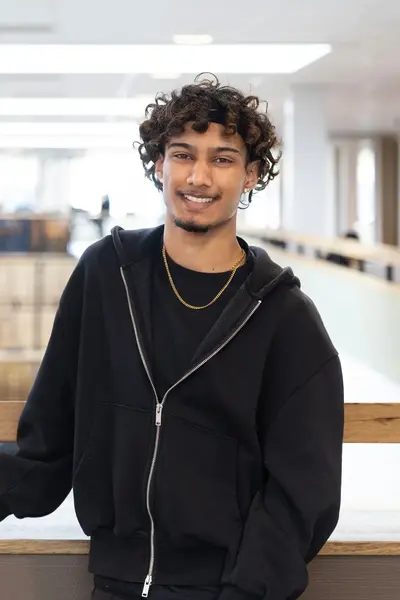 Student met zwarte hoodie glimlacht naar de camera. 