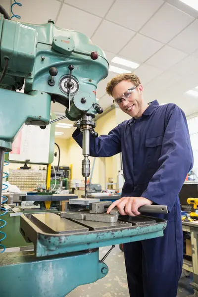 Jongen in overall staat achter boormachine.