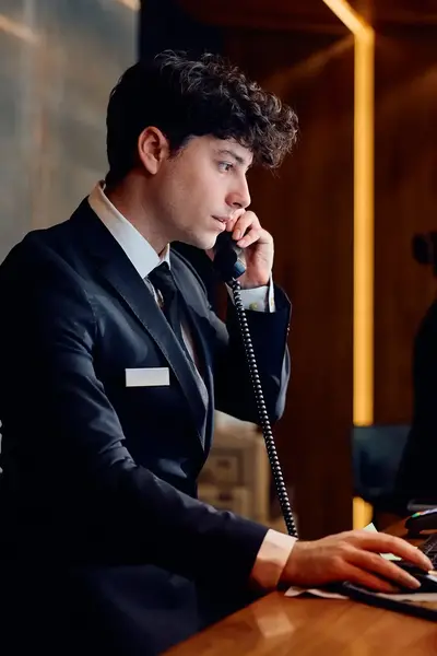Student in pak achter hotelreceptie beantwoordt telefoon in bijzijn collega's.
