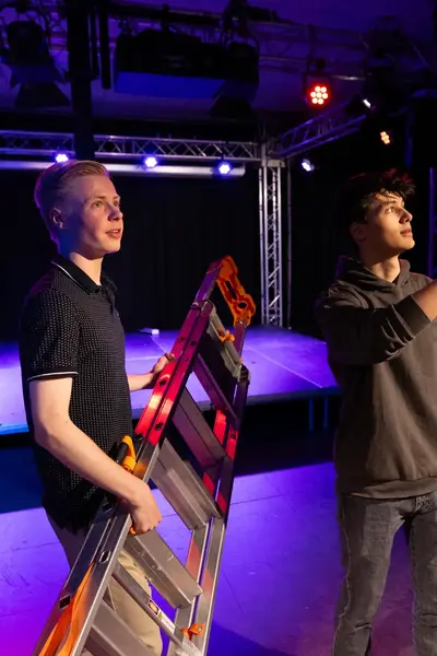 Twee studenten met een trap in een studio, één student wijst omhoog.