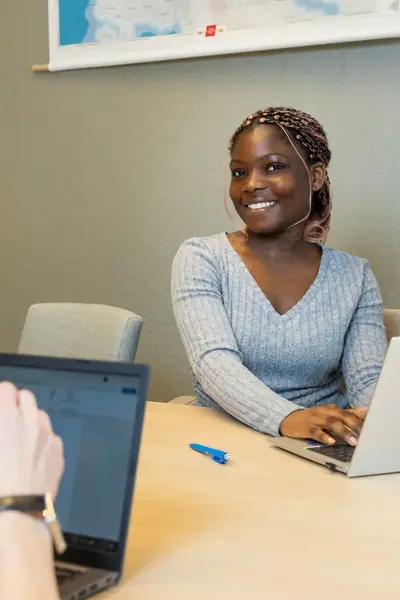 Twee studenten werken samen aan tafel met laptops tijdens een overlegmoment op kantoor.