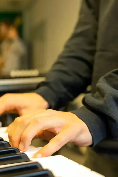 Student bespeelt een keyboard tijdens een bandrepetitie, met medestudenten op de achtergrond.