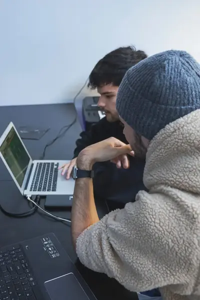 Twee studenten werken samen aan een productie met laptops, audiokabels en mengpanelen.
