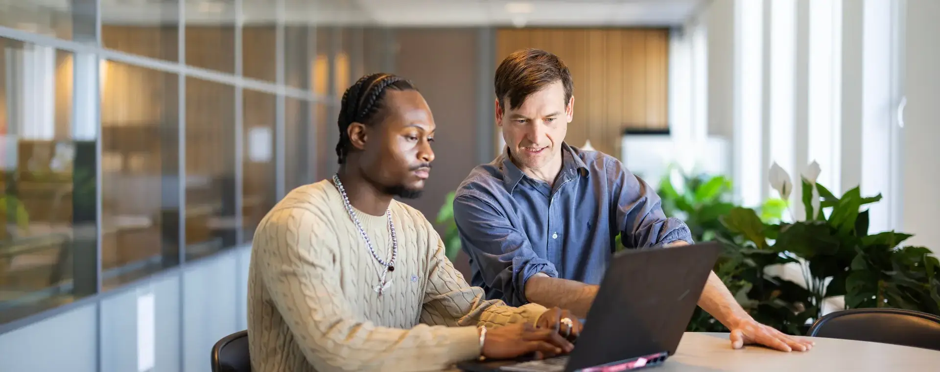 twee jongens achter laptop aan een ronde tafel