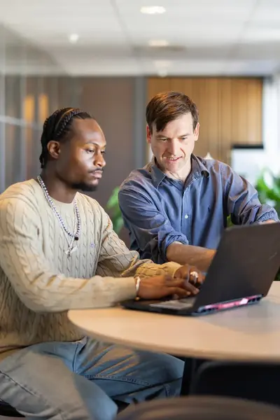 Twee mannen achter laptop aan een ronde tafel.
