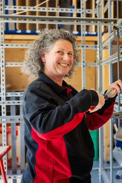 Een vrouwelijke docent Elektro & Installatietechniek staat in een praktijk lokaal bij een wand waar stopcontacten en elektro punten hangen om mee te oefenen en laat zien hoe het werkt.