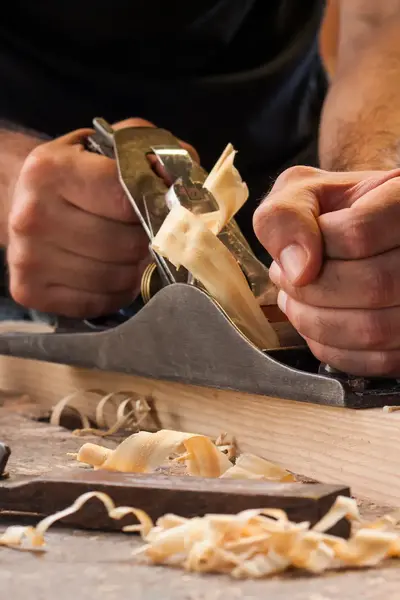 Twee handen die een plank schaven omringd door houtkrullen