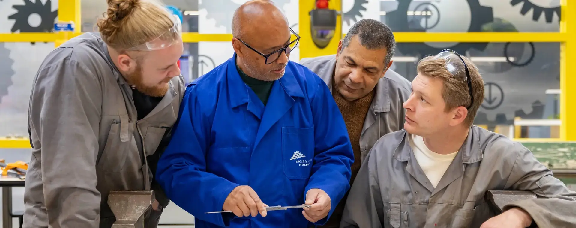 Docent omringd door deelnemers legt de lesstof uit