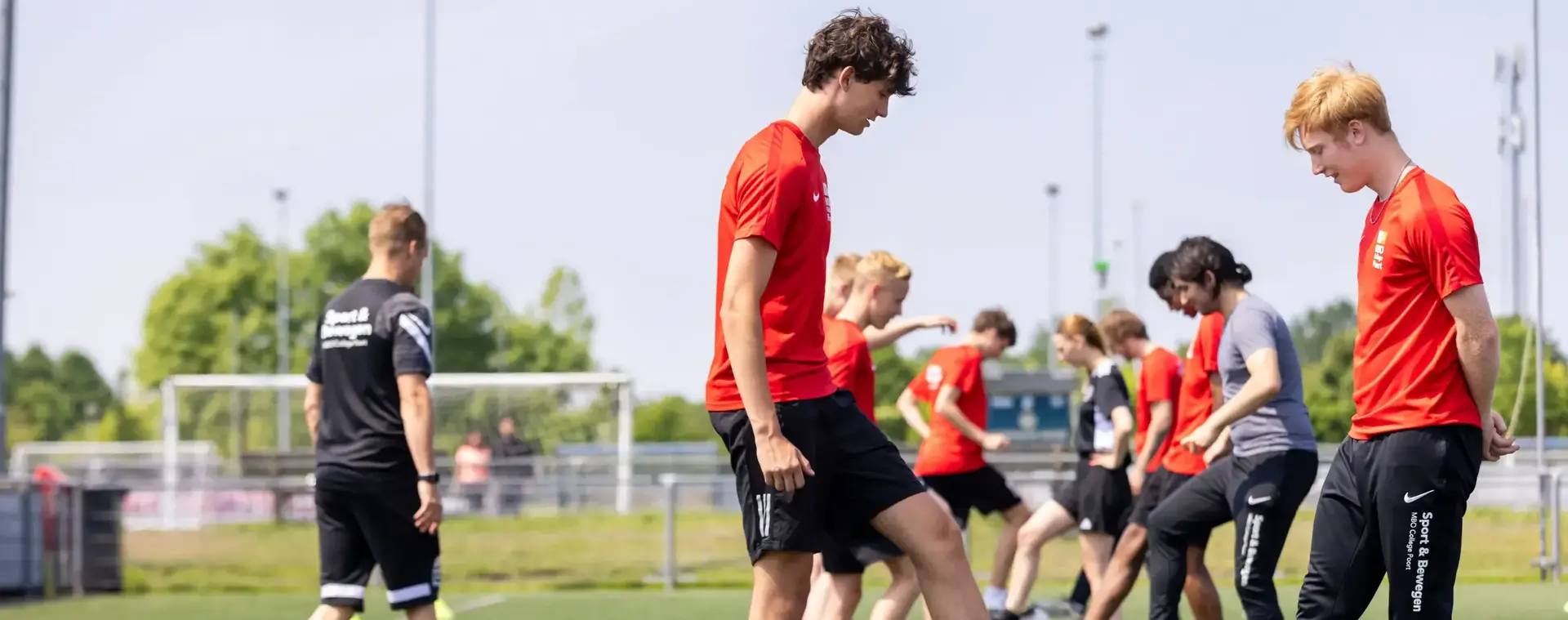 Een trainer/docent laat studenten sport op een sportveld buiten voetbaloefeningen doen.