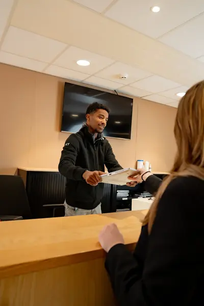 Jongeman overhandigt laptop aan collega vanachter een balie