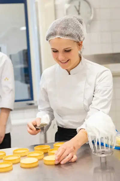 Studenten in de bakkerijopleiding werken samen aan het vullen van tartelettes met een crèmevulling.