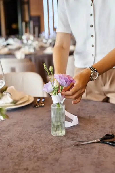 Vrouw die vaasje met bloemen schikt op een dinertafel.
